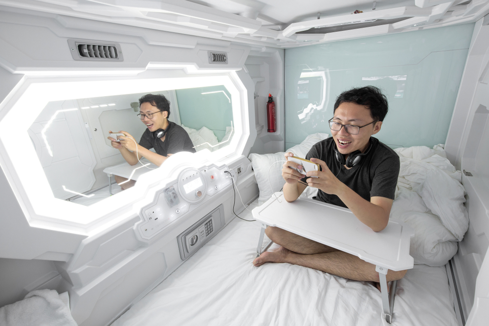 A man in a unique hotel  that is a white cubicle with a bright light and a mirror in a hotel while traveling in Japan