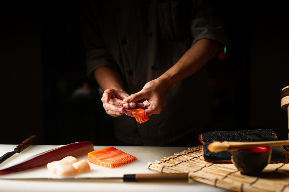 Closeup of hands making a sushi roll out of fresh salmon