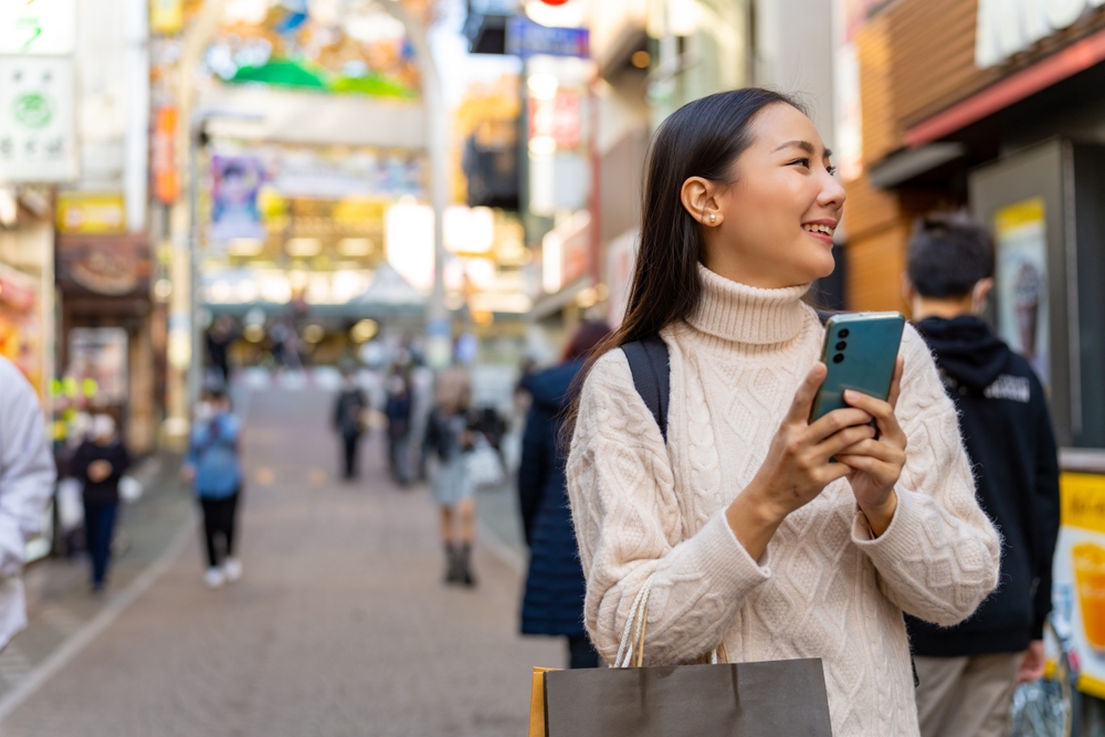 A young Asian woman holding a cell phone while walking the streets traveling in Japan