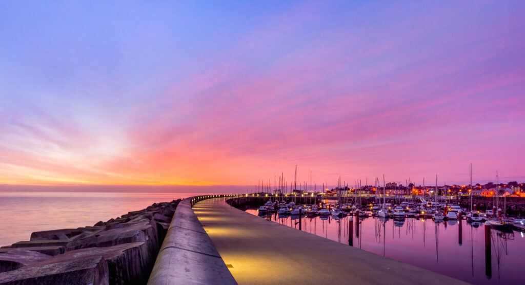 Amazing sky on sunrise at Greystones yacht marina or harbour with anchored boats and long illuminated pier. One of the things to do in 3 days in Dublin.