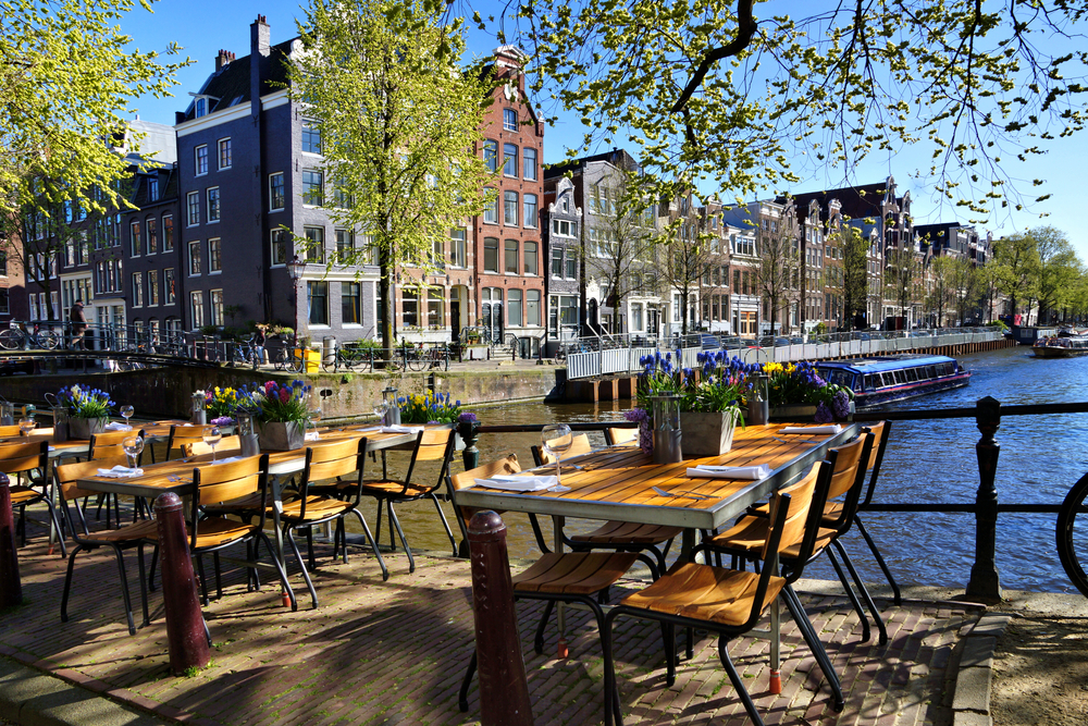 Outdoor tables at a cafe overlooking a canal on a sunny day.