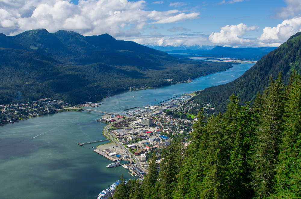 Looking down from a green mountain to Juneau nestled against the water on a sunny day.