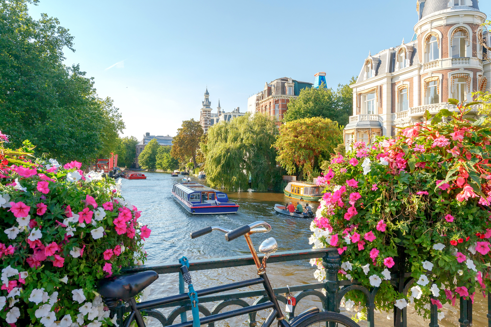 View of a canal with a boat from a bridge with flowers and a bike.