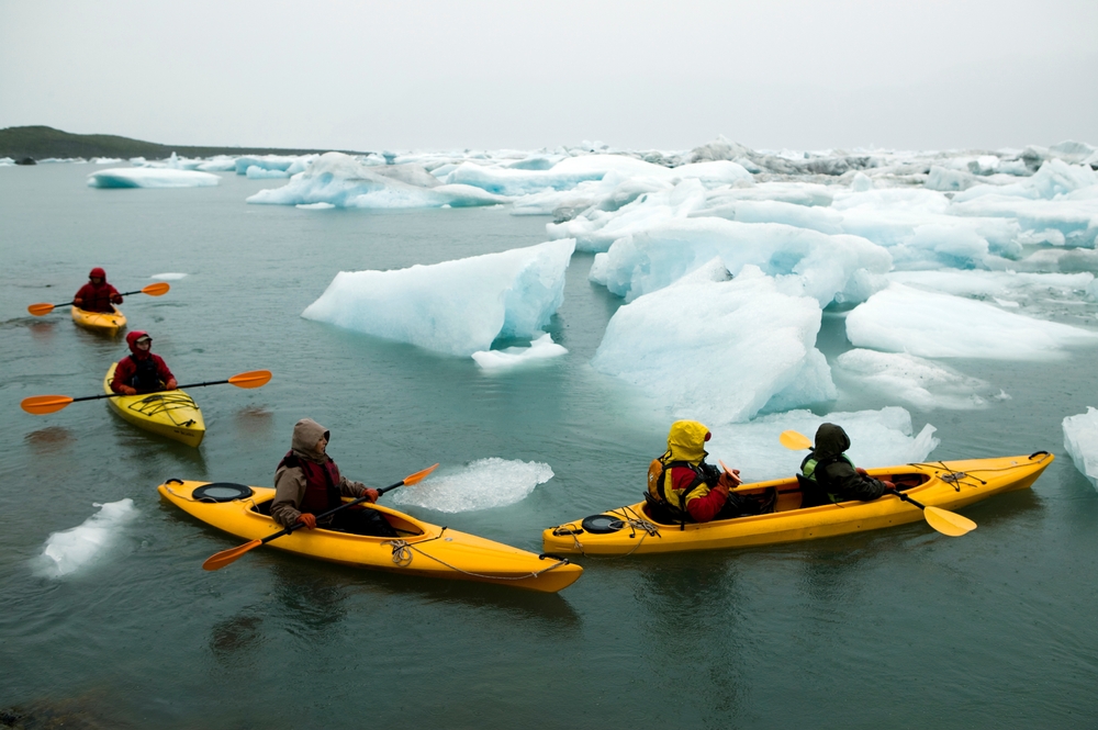 People bundled up in yellow kayaks paddling through icebergs on a cloudy day.