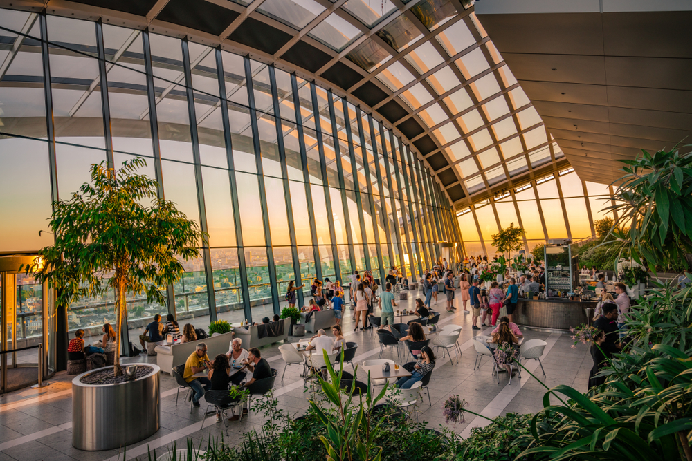 View of sunset over London from floor to ceiling windows in the Sky Garden with a cafe and many plants.