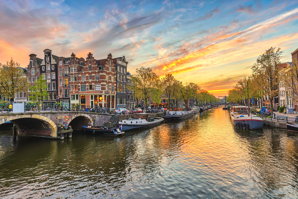 Sunset over the canals of Amsterdam featuring boats, a bridge, and canal houses.