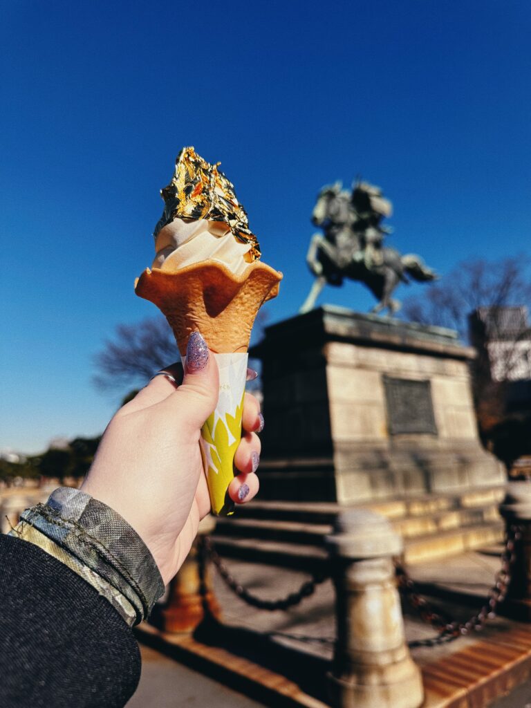A woman's hand holding an ice cream cone with vanilla ice cream that has gold leaf sheets on it one of the most unusual things to do in Tokyo
