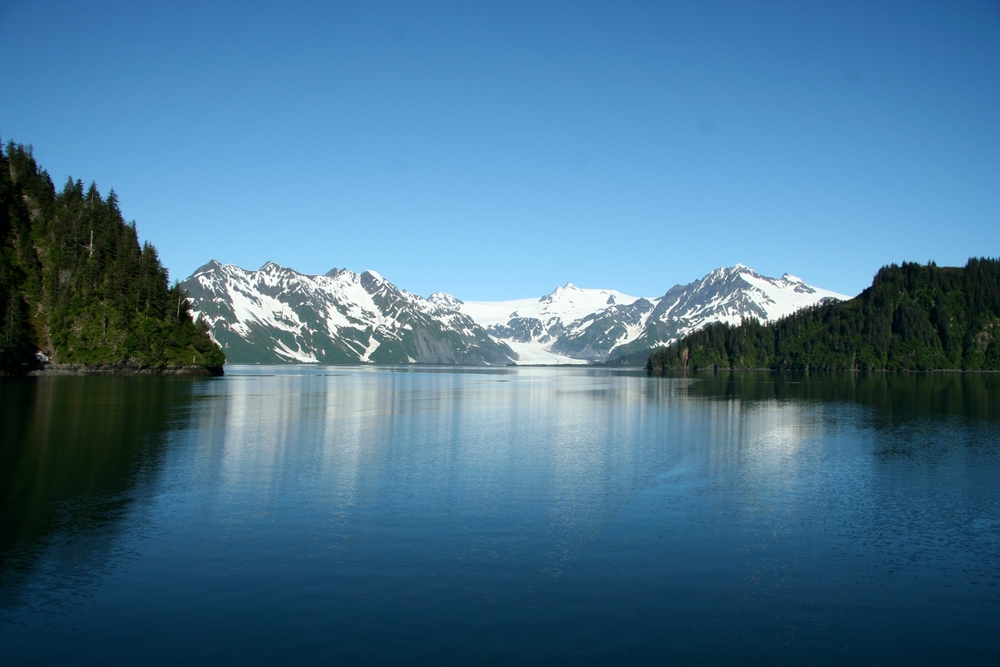 Calm blue water in foreground with glacial mountains in background