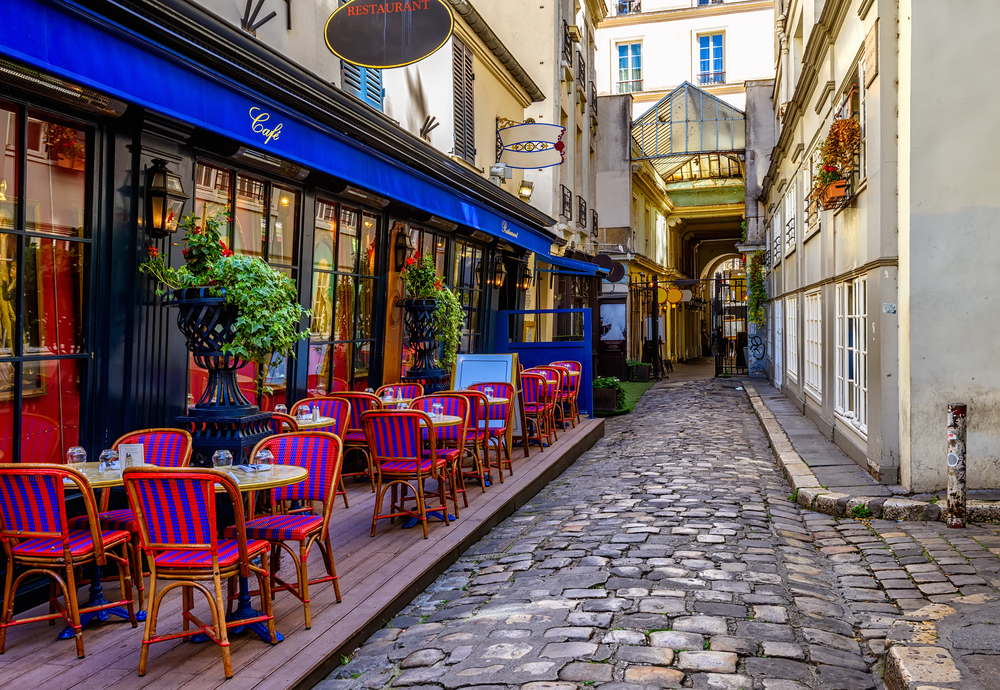 Colorful, striped chairs at table outside of a cafe on a small, cobblestone street in Paris.