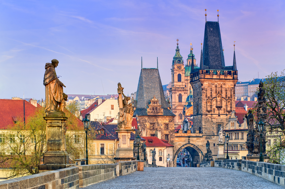Early morning on an empty Charles Bridge with statures and a historic gate.