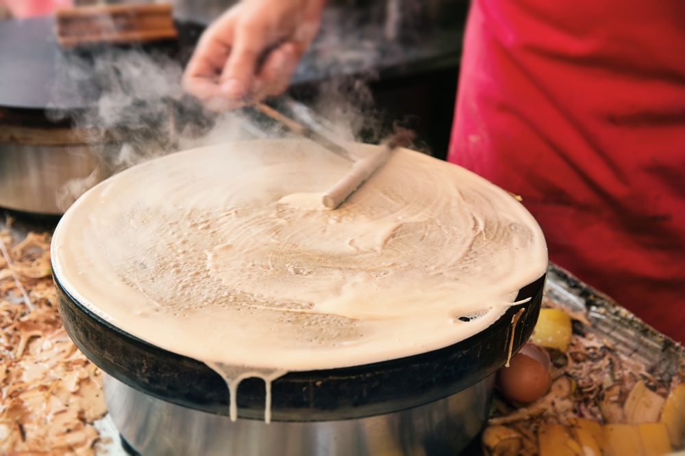 A person making a crepe with batter on a round skillet. during 4 days in Paris itinerary
