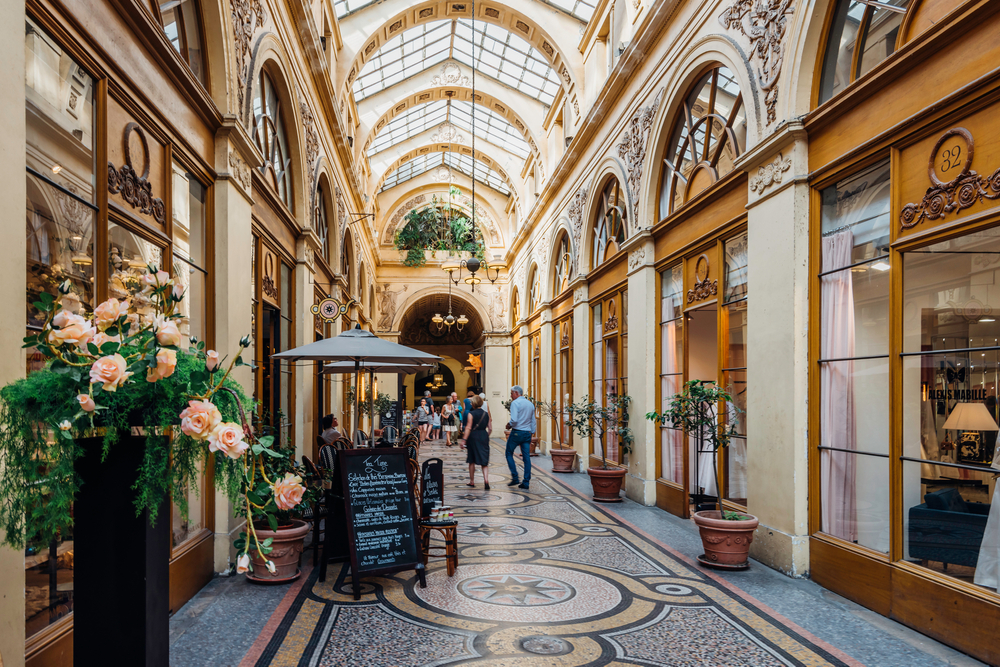People walking down the Galerie Vivienne covered passage with a glass ceiling and many shops and restaurants.