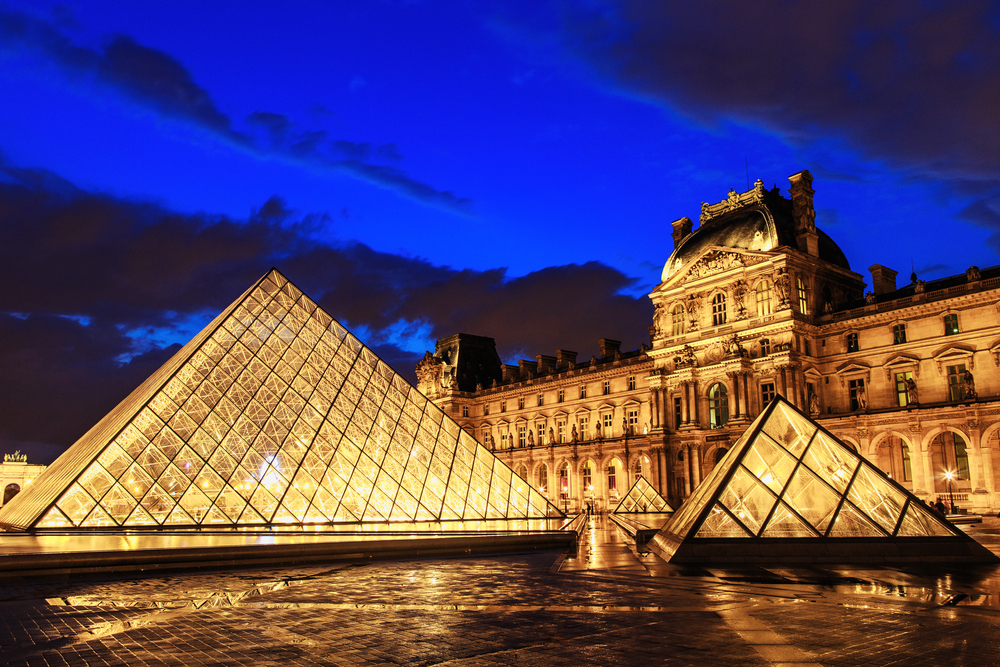 Night at the Louvre Museum with the building and glass pyramids lit up.