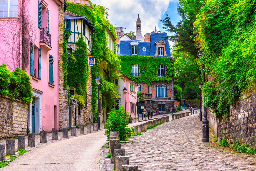 Pink and stone buildings covered in ivy on a cobblestone road in Montmartre during 5 days in Paris.