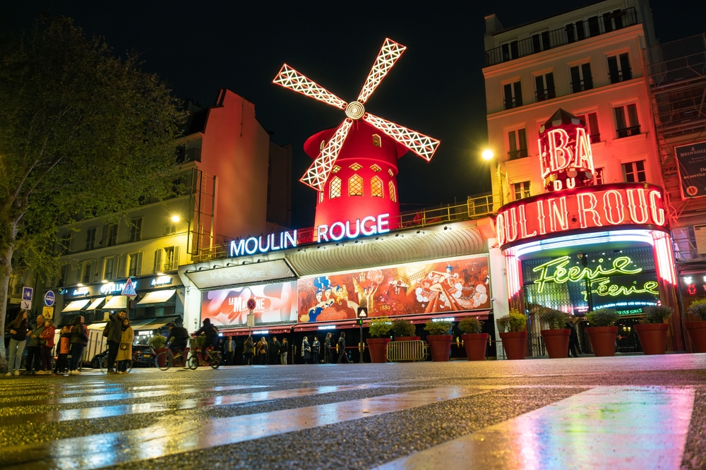 Lit up red windmill over the Moulin Rouge at night.