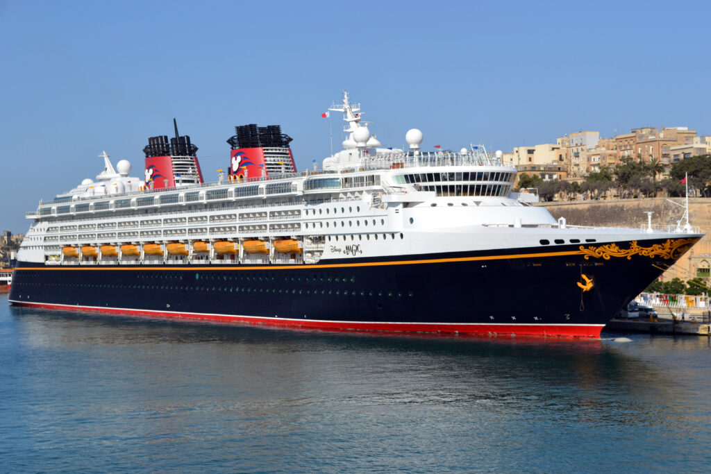 blue Disney  cruise ship with white trim and red stacks in port