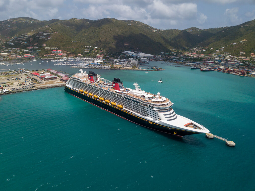 Disney cruise  ship sailing from port through turquoise waters with mountains in the background
