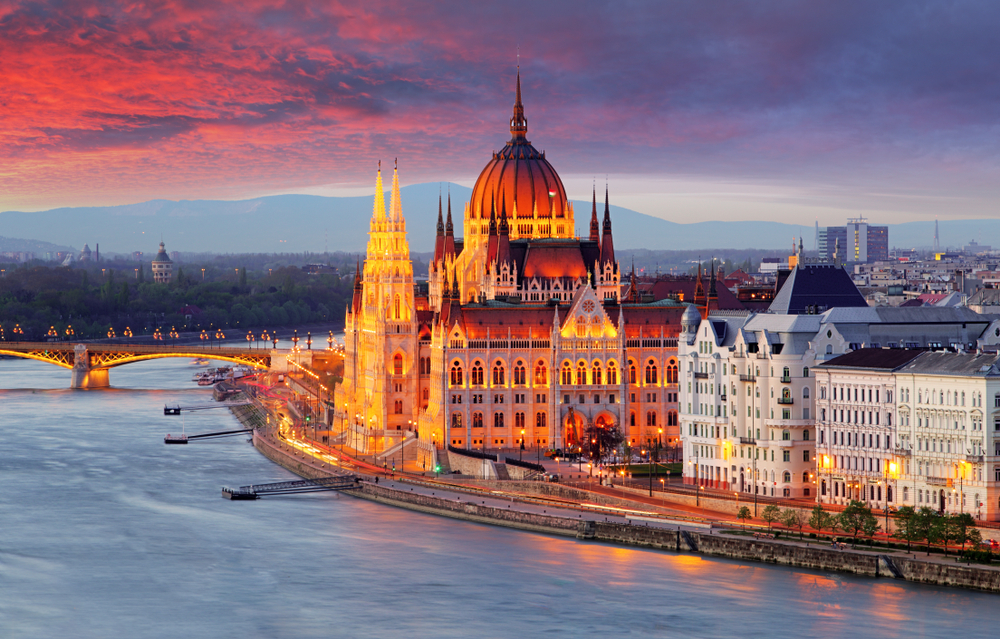 city beside a river with mountains in the backdrop at sunset traveling to budapest