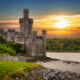castle beside a river surrounded by greenery while the sun sets traveling to ireland