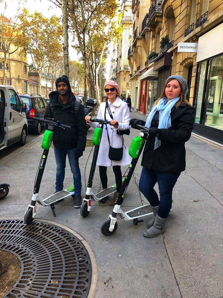 Two young woman and a young man standing with Lime e-scooters on the sidewalk during 2 days in Paris.