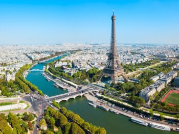 Aerial photo of Paris featuring the Eiffel Tower standing over the Seine River on a sunny, clear day.