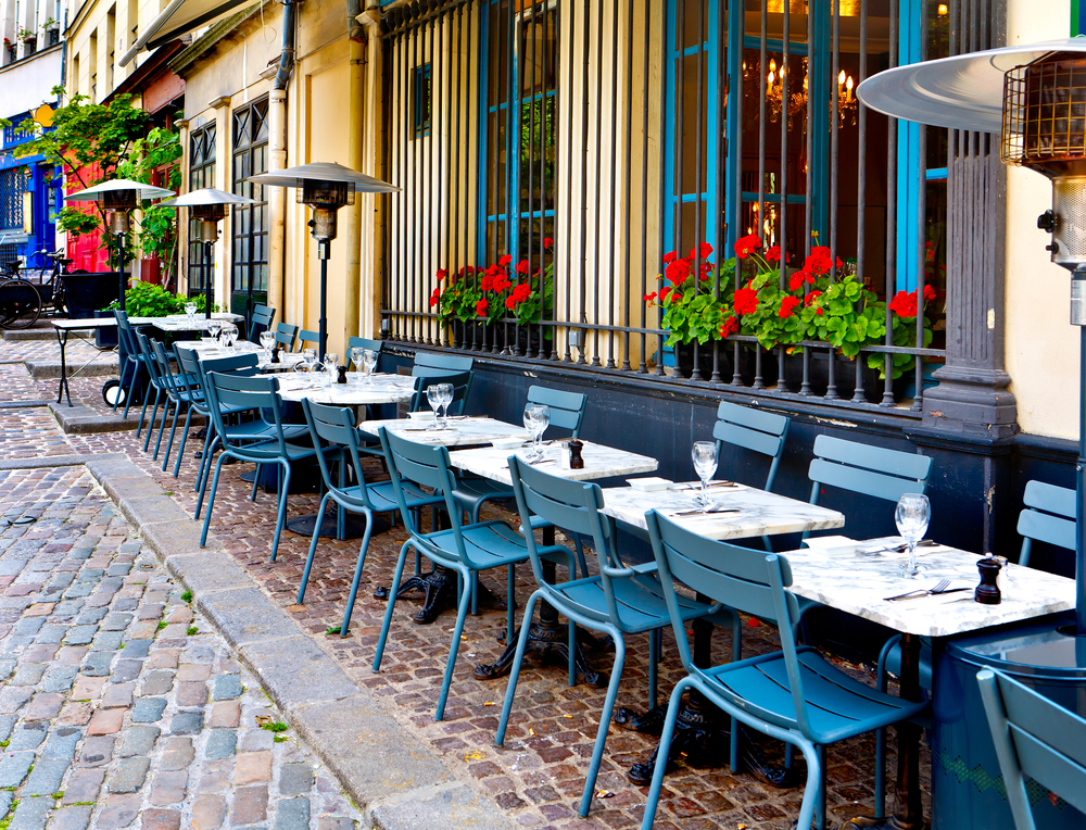 Line of white tables with blue chairs outside of a cafe in Paris.