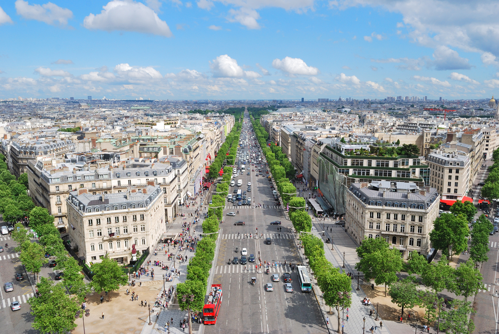 Sunny day looking down over the tree-lined Champs Elysees with many cars and people walking around.