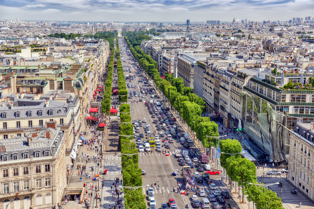 View looking down the tree-lined Champs-Elysees with lots of cars and people walking on the sidewalks.