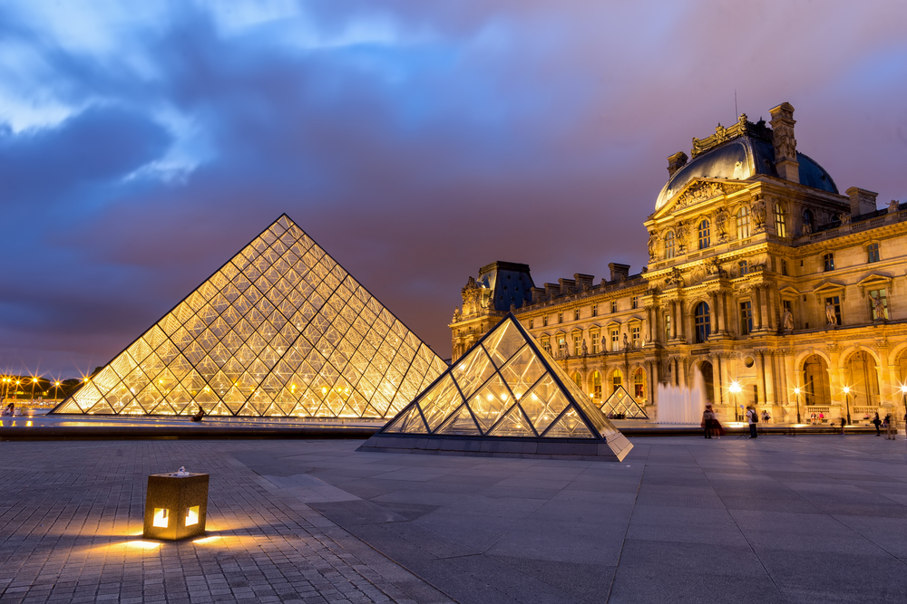 Purple dusk over the lit up Louvre Museum with the iconic glass pyramids.