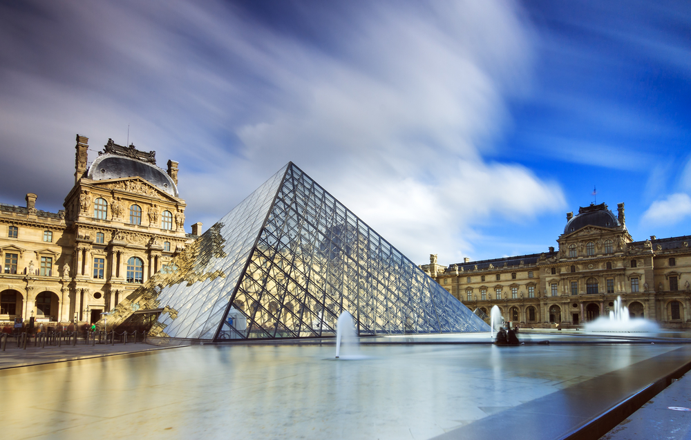 Partly cloudy day over the glass pyramid and former palace of the Louvre Museum.