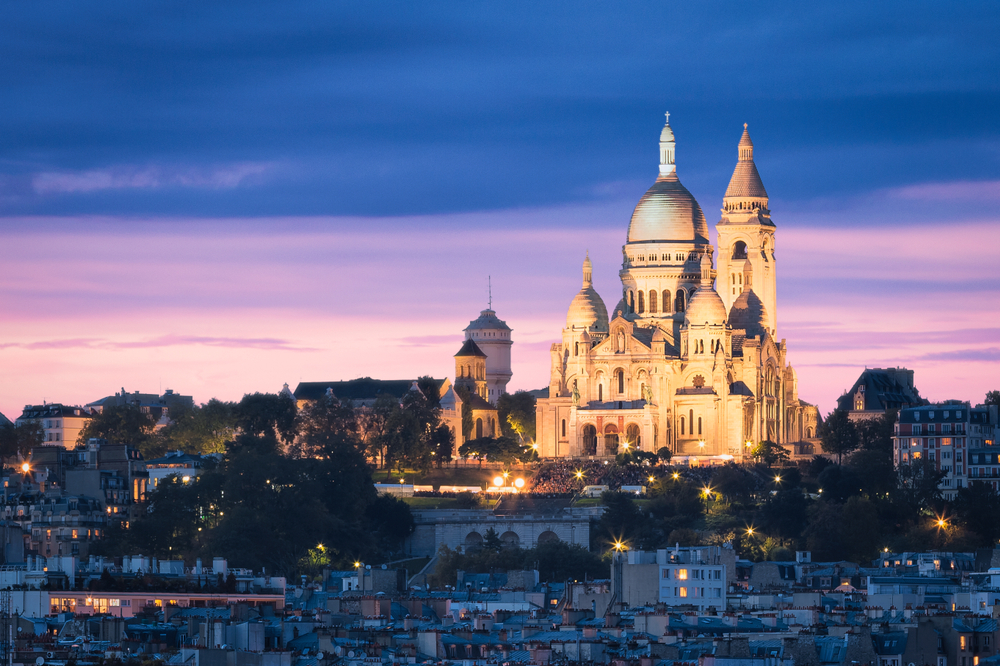 Vivid purple sunset over the lit-up Sacre-Couer Basilica towering over the Montmartre district.