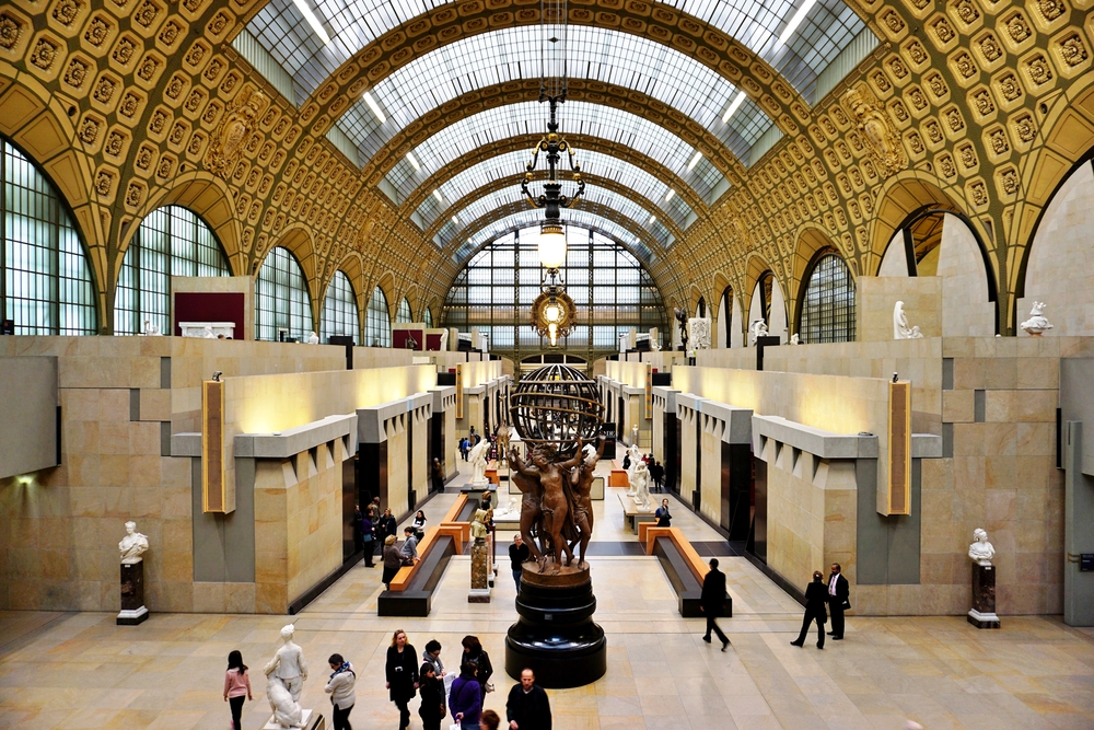 Inside the Musee d'Orsay with a cylinder ceiling with skylights, many statues, and people walking around.
