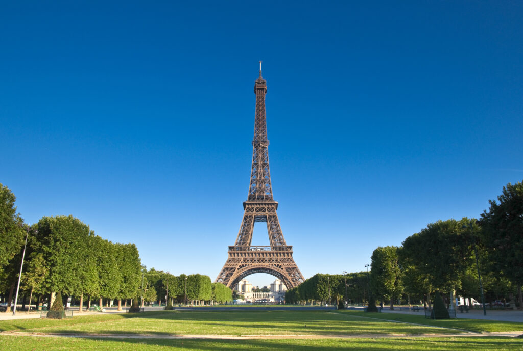 Eiffel Tower in middle with green trees on either side with green grass in foreground