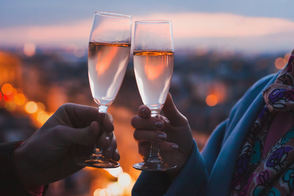 Close-up of couple clinking two glasses of champagne on a rooftop bar in the evening ending one day in Paris.
