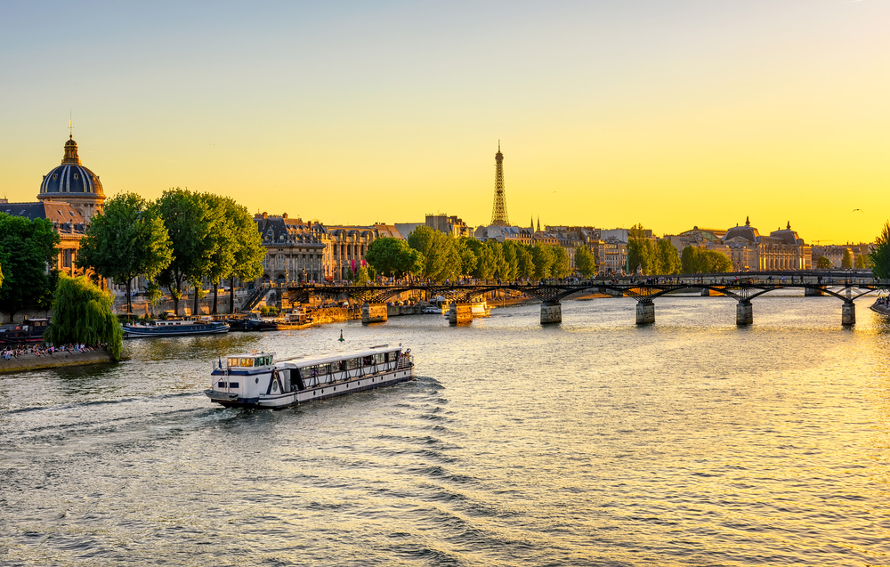 Yellow sunset over the Seine River with a cruise boat and the Eiffel Tower in the distance.