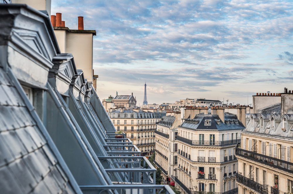 View from a balcony over looking the rooftops of Paris with the tip of the Eiffel Tower in the distance on a London-Paris itinerary.