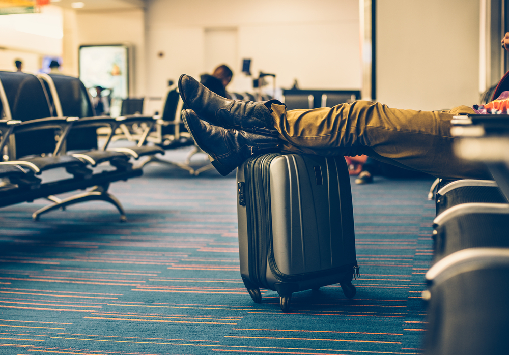Solo senior travel tips include carryon at airport with legs/boots stretched out over the top.