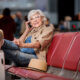 Solo senior travel tips show grey haired woman sitting on red couch talking on phone