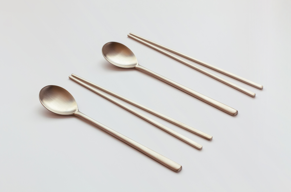 Two sets of metal chopsticks and spoons on a plain, white background.
