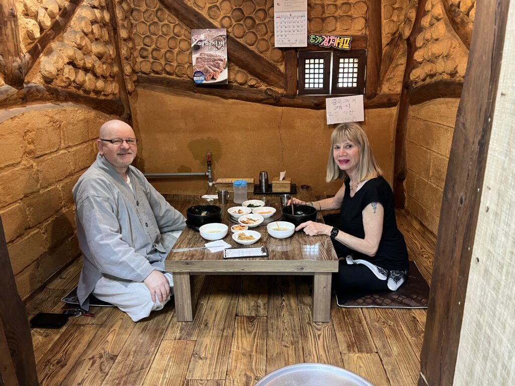 Man and woman sitting on the floor at a table with bowls of Korean food.