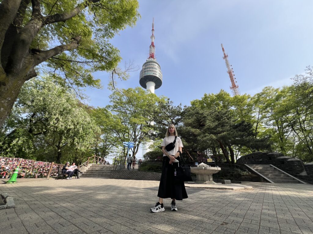 Woman standing in front of green trees and the N Seoul Tower while traveling in South Korea.