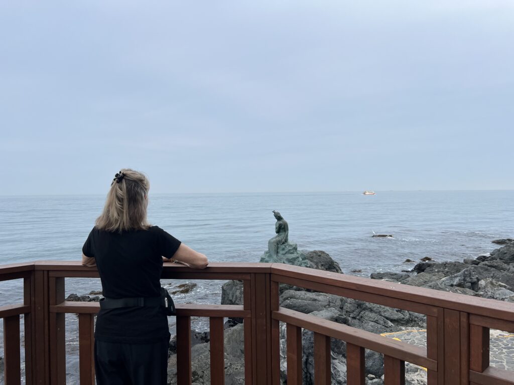 Woman looking out over the ocean and a stone mermaid statue on a cloudy day.