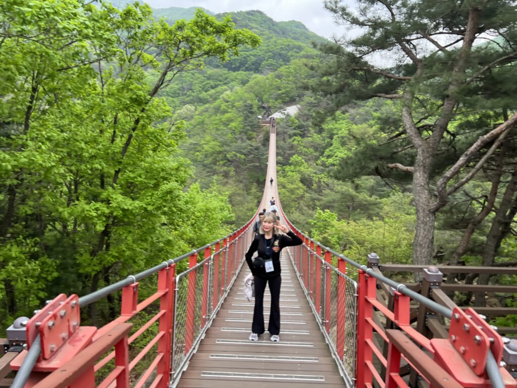 Woman posing on a red and brown suspension bridge among trees while  traveling to South Korea.