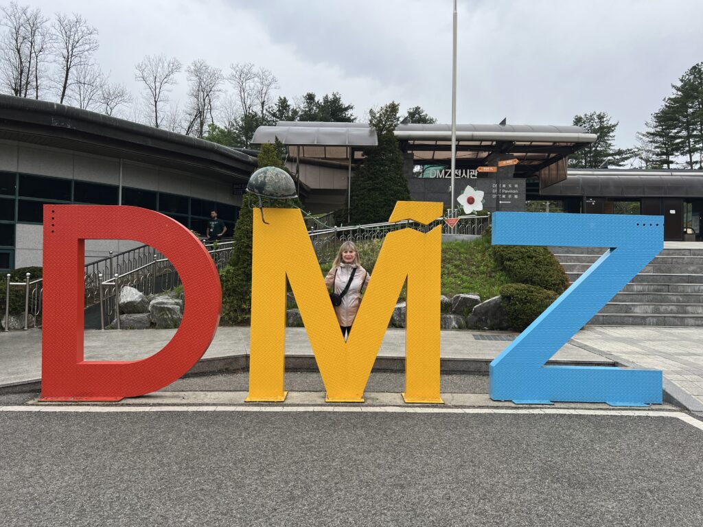 Woman posing with the colorful sign for the DMZ on the border of South Korea.
