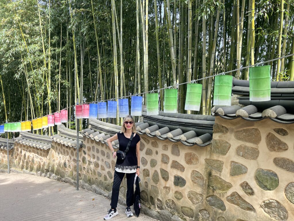 Woman posing in front of a stone wall and colorful hanging lanterns next to a bamboo forest.