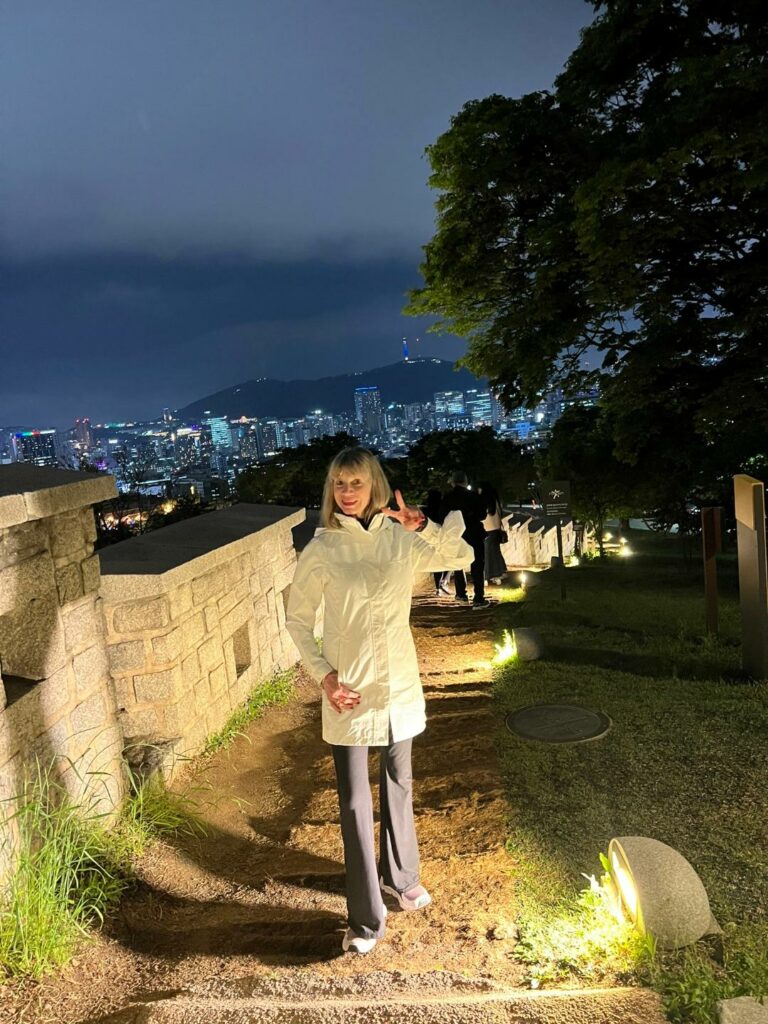 Woman walking on a path at night with the Seoul skyline in the background.
