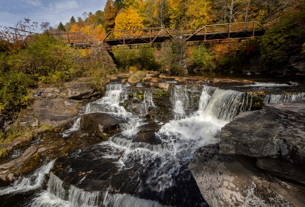 cascading water with a bridge behind it surrounded by fall foliage