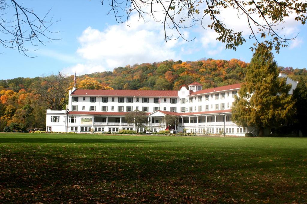 White hotel in front of some mountains with a large lawn. It is fall and the tress are changing color.  