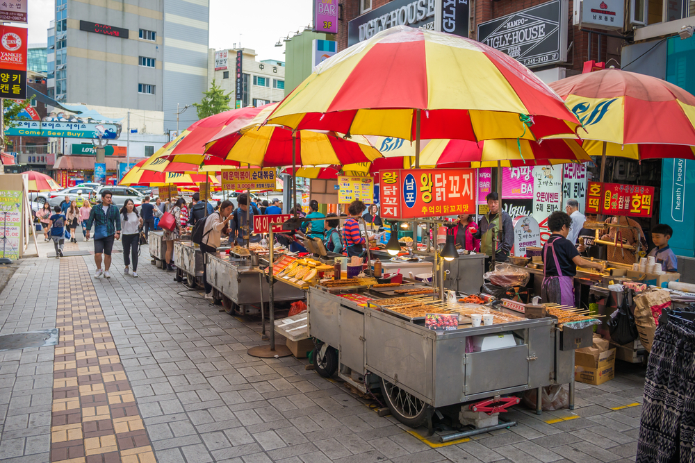 A group of food stalls with orange and red umbrellas over them in BIFF Square, one of the best places to visit in Busan.