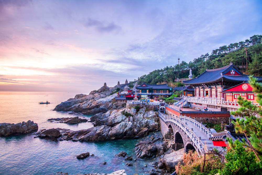 Purple and pink sunset over the rocky coastline and the traditional Haedong Yonggungsa Temple, one of the best places to visit in Busan.